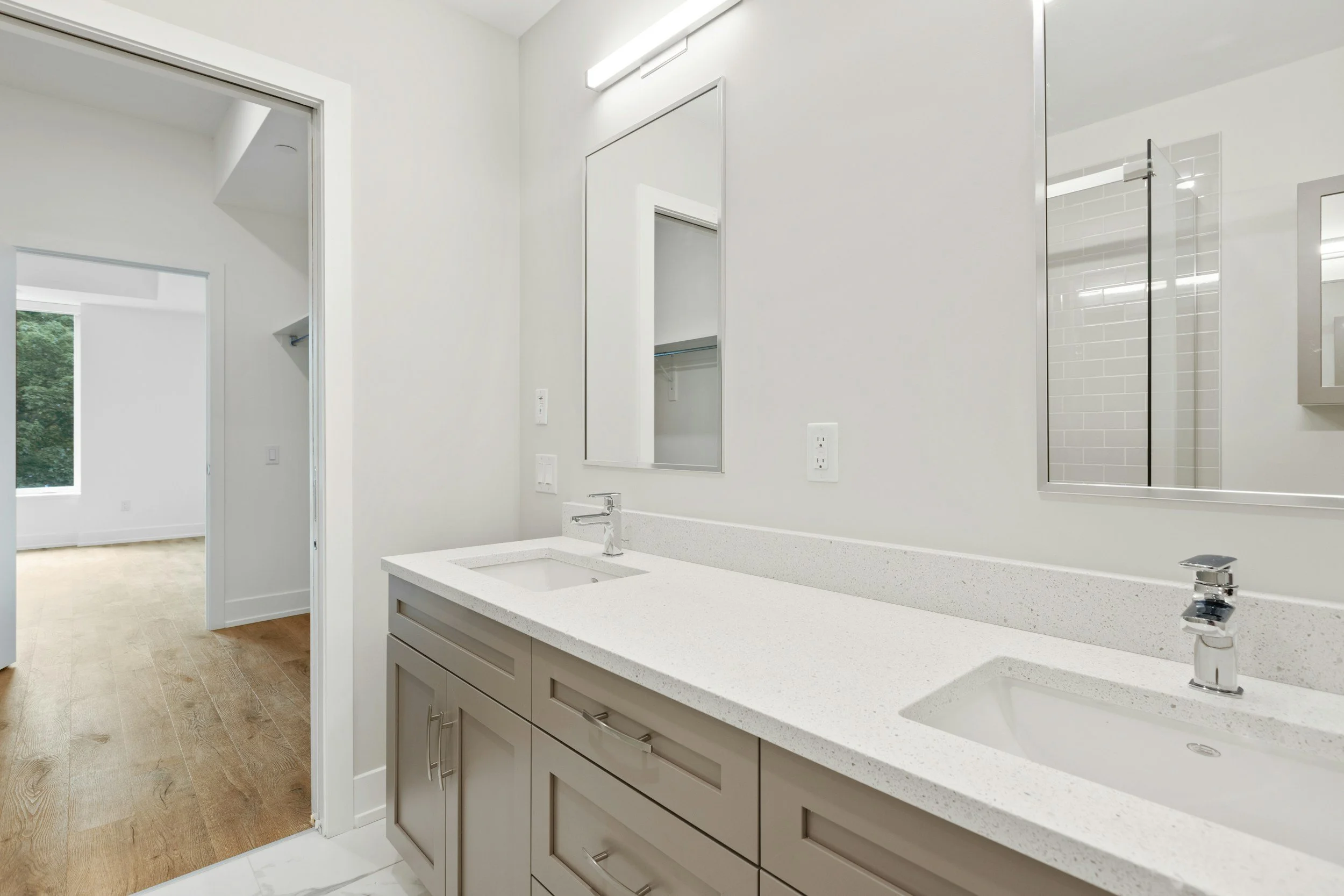 Double bathroom vanity with two sinks, a large mirror, and a white countertop, in a modern bathroom with white walls and visible shower area.