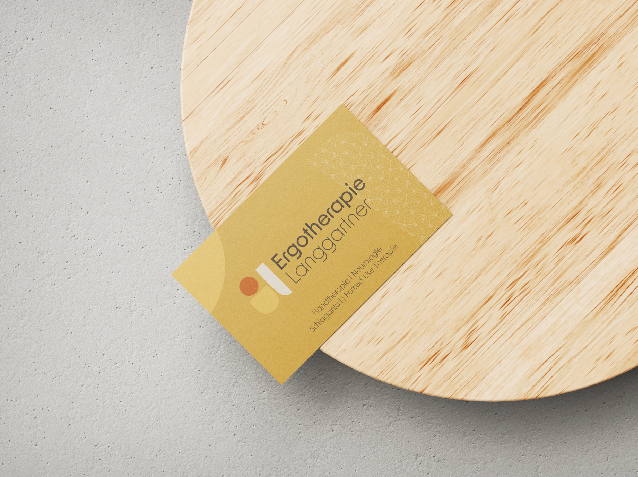 Visitenkarte auf einem runden Holzbrett, Text 'Ergotherapie Langgartner', beige mit geometrischem Muster.