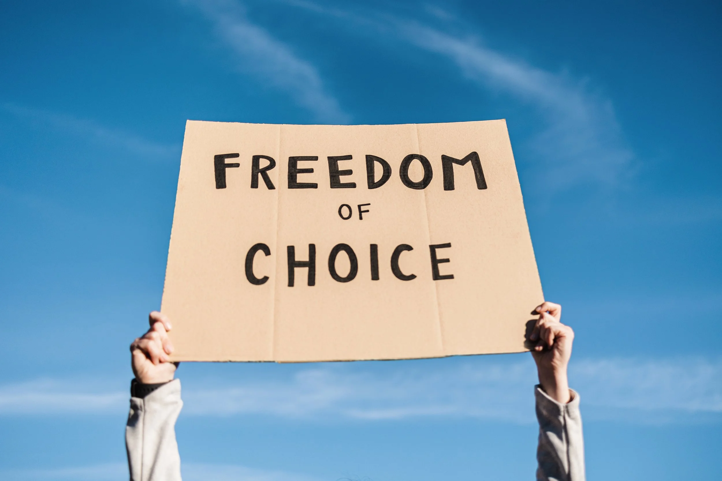 Person hält ein Plakat mit der Aufschrift 'Freedom of Choice' gegen einen blauen Himmel.