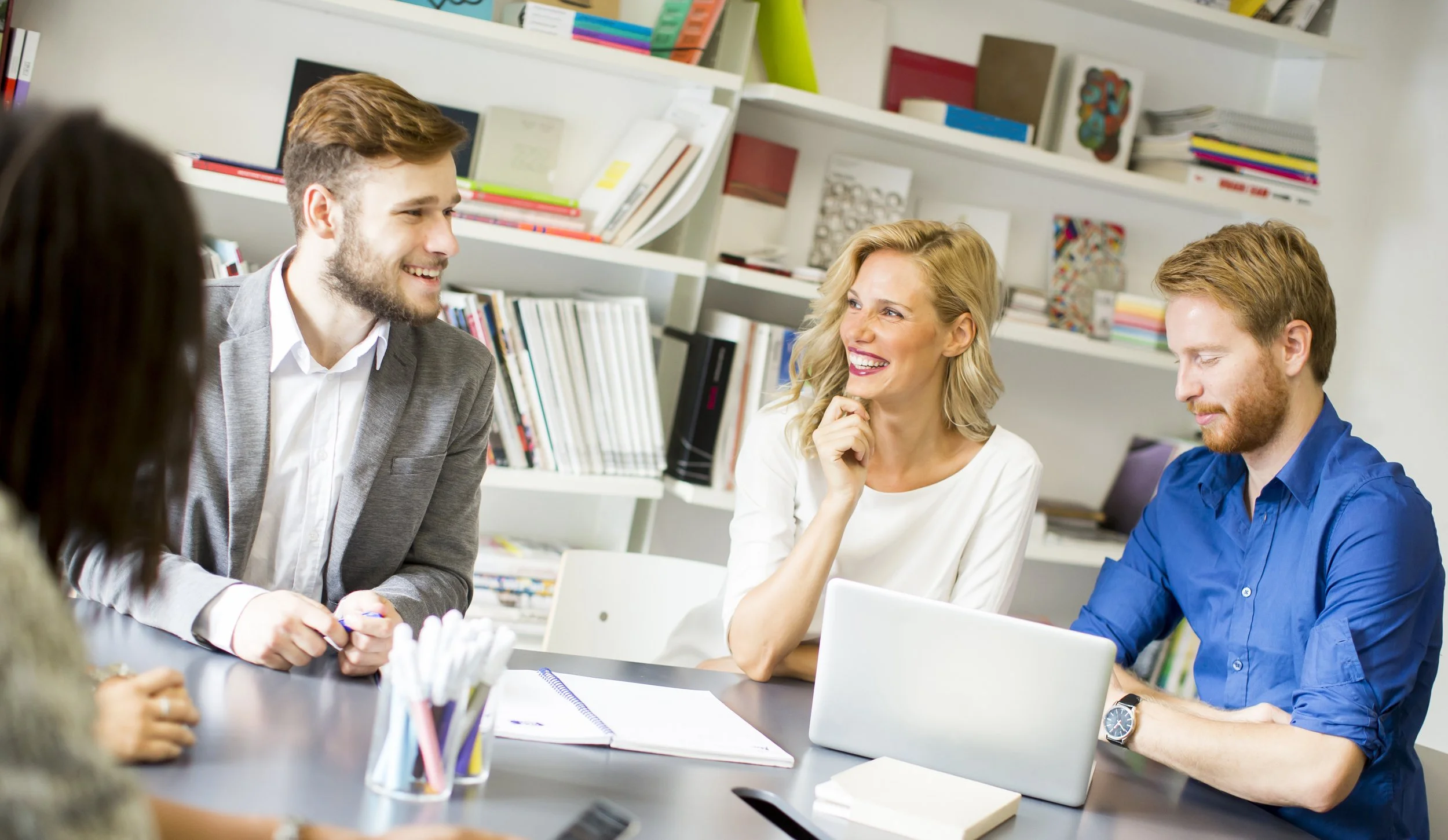 Fünf Menschen sitzen an einem Tisch in einem Büro, lachen und unterhalten sich.