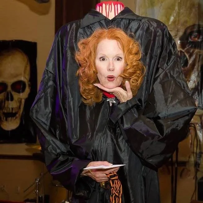 Person in a headless costume with red hair, surrounded by Halloween decorations, including skulls.