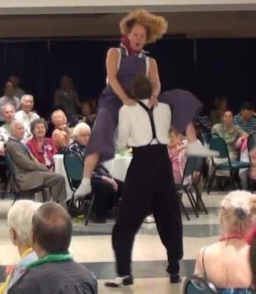 A man and woman swing dancing in a room with an audience seated around them.