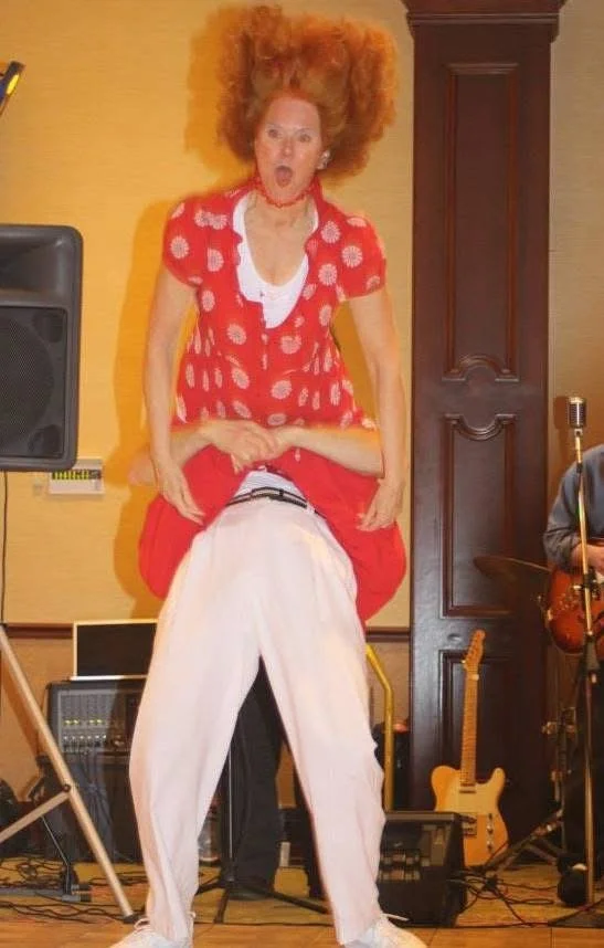 Woman in a red dress being lifted by a man during a dance performance, surrounded by musical instruments.