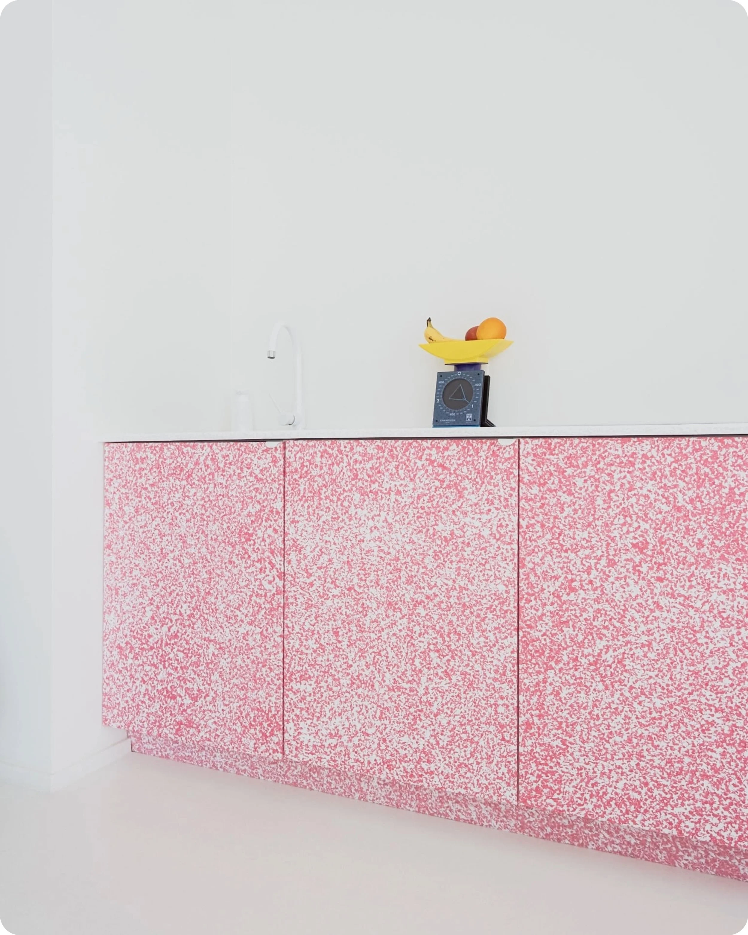 Plein cadre de la cuisine du showroom de Kooloo Modern, construite à partir de plastique recyclé HDPE de couleur rose et blanche, atmosphère très minimaliste et design avec objets design et une plante verte au sol en avant plan.