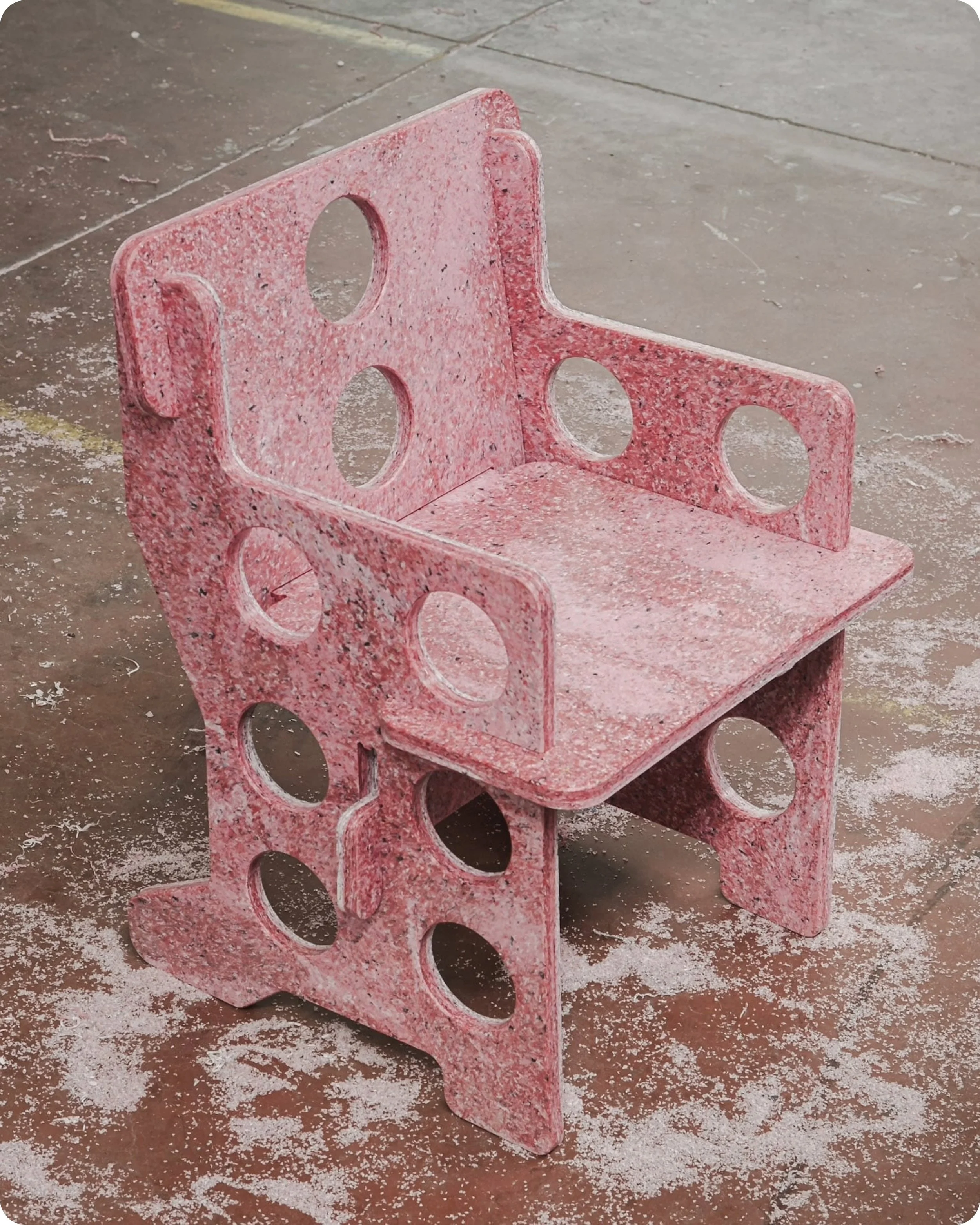 Chaise en plastique recyclé rose et blanche réalisée à partir du design de Lionel Jadot prise de trois quart face en plongée, posée sur un sol industriel de couleur orange avec poussière de découpe au sol.