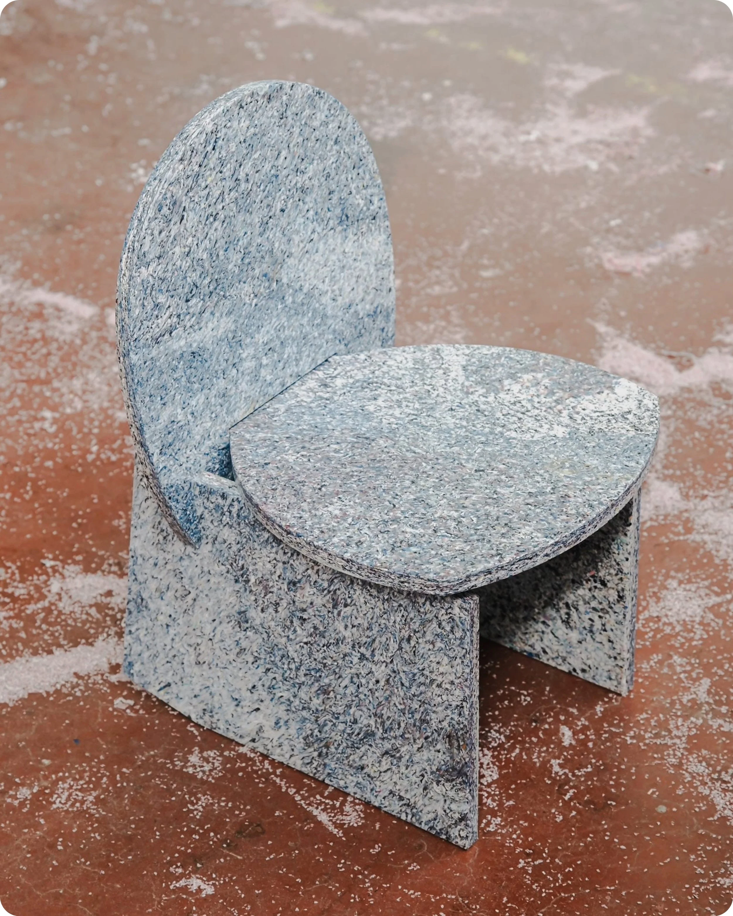 Chaise en plastique recyclé bleu et blanc réalisée à partir du design de House of RoRo, prise de trois quart face en plongée, posée sur un sol industriel de couleur orange avec poussière de découpe au sol.