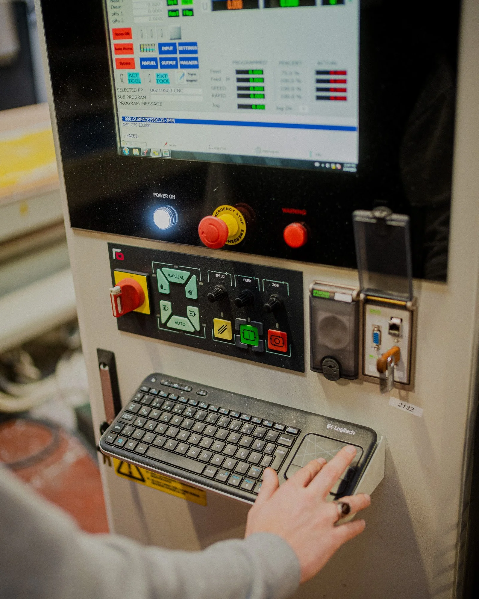 Plan serré en plongée d'une main humaine qui enfonce des boutons de programmations d'une machine de découpe numérique CNC 3 axes