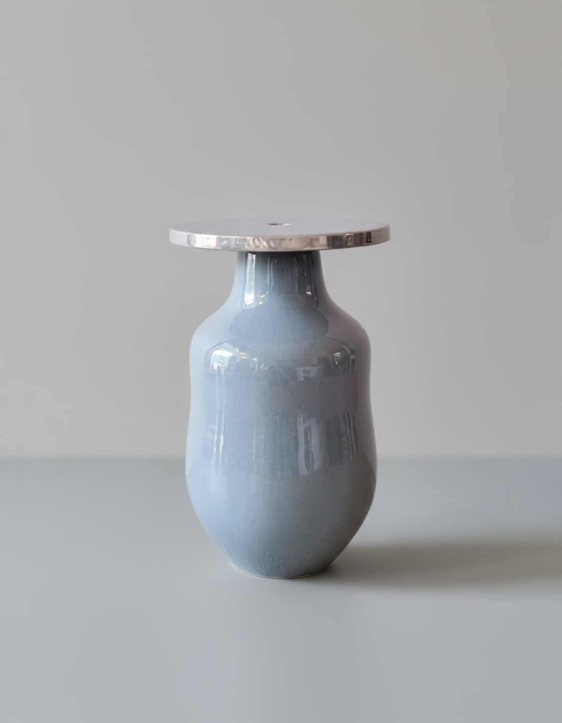 Vaso di ceramica di colore grigio con forma snella e collo largo, sopra un piano bianco, sullo sfondo una parete chiara