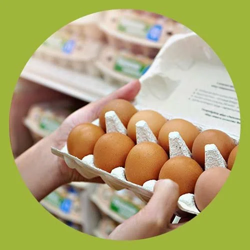 Person holding a carton of brown eggs in a grocery store aisle.