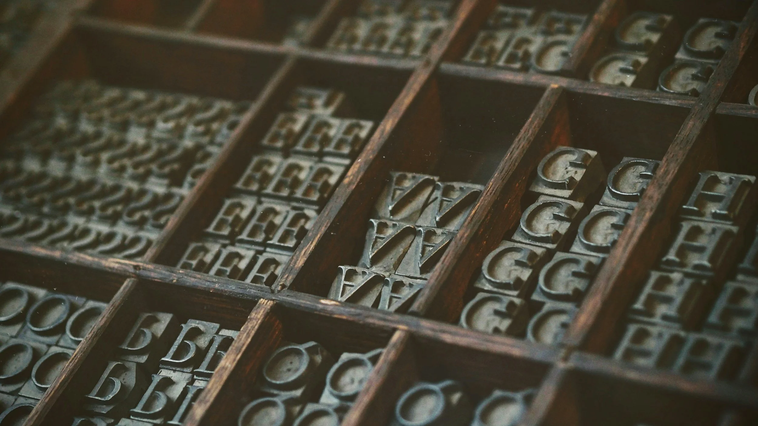 Vintage metal letterpress types arranged in a wooden type case with individual compartments.