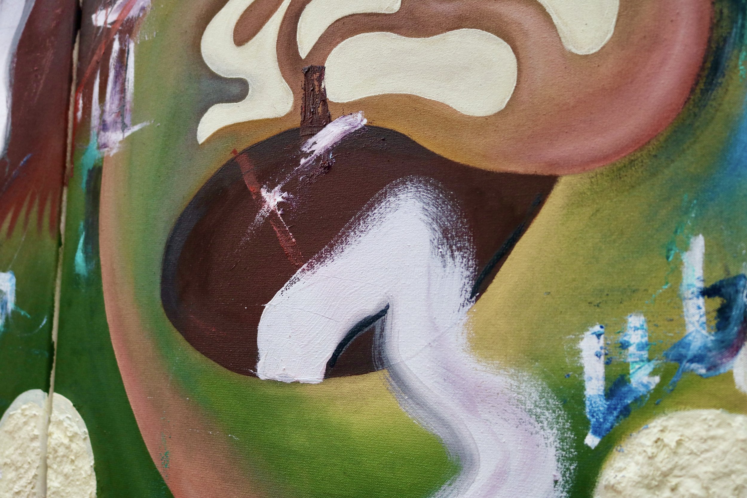 Close-up of abstract graffiti art on a wall, featuring various colors including brown, white, green, pink, and blue. The painting includes swirling patterns and brushstrokes, with some areas showing texture from thick paint application.
