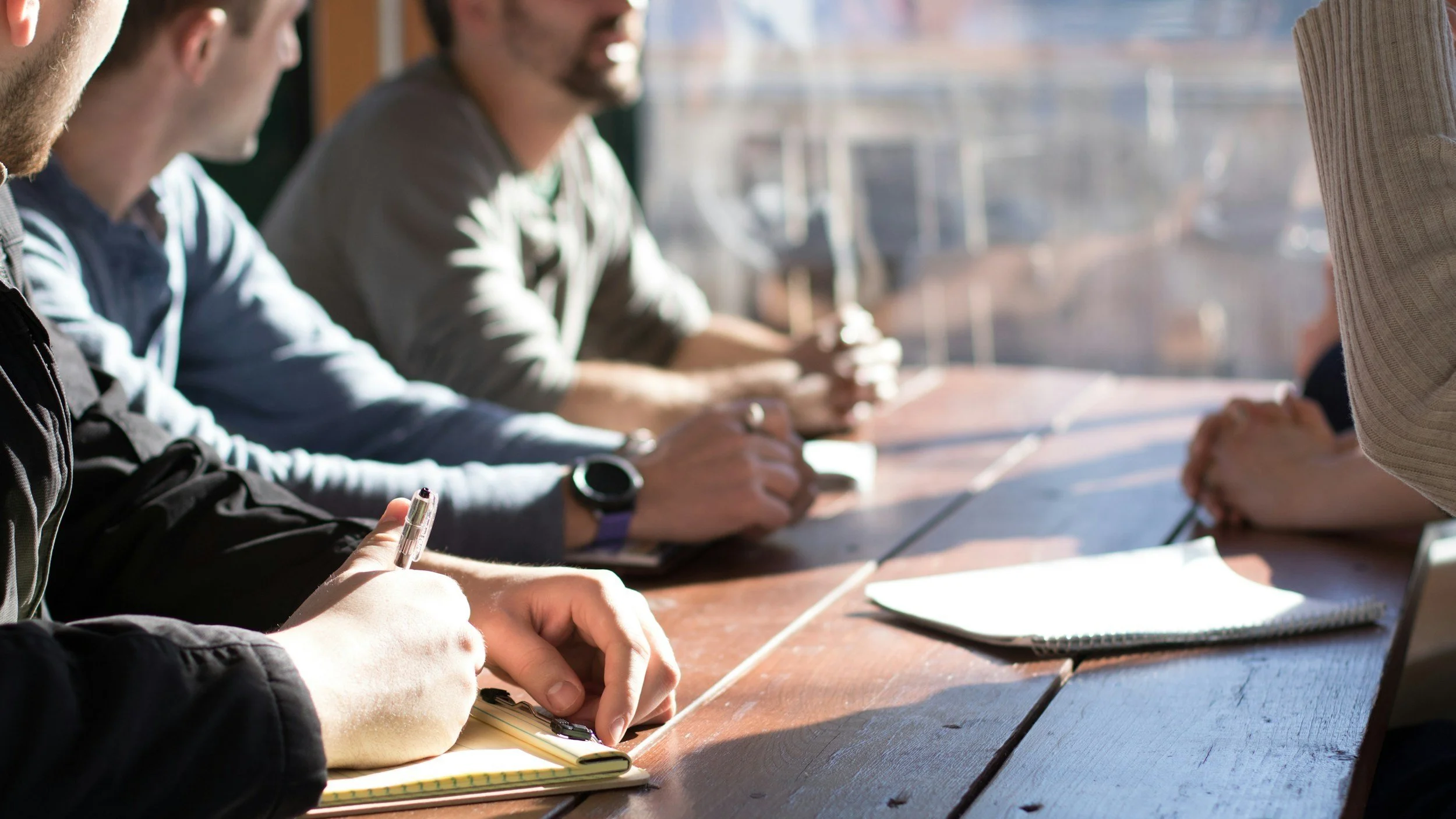 Team members sat around a table holding pens and notebooks in a meeting or discussion.
