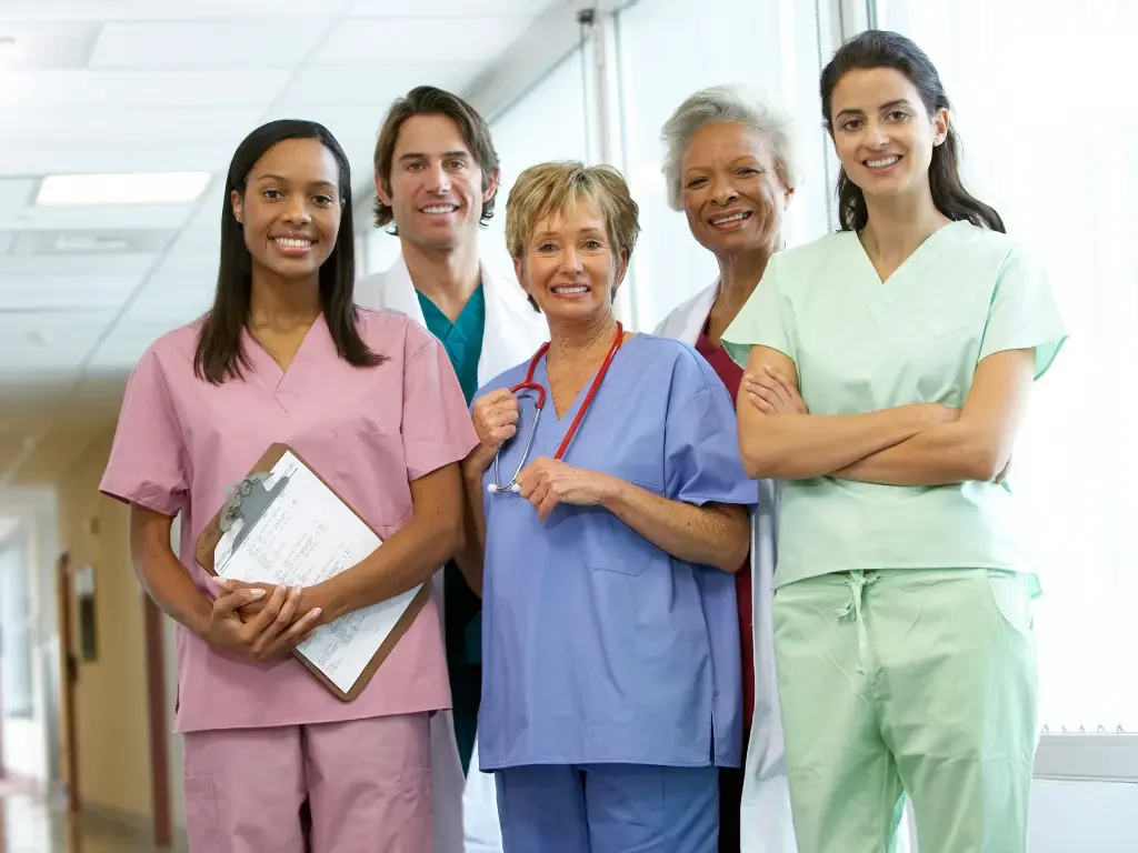 Smiling staffing nurse team of diverse healthcare professionals standing together in a hospital corridor, wearing scrubs and medical uniforms.