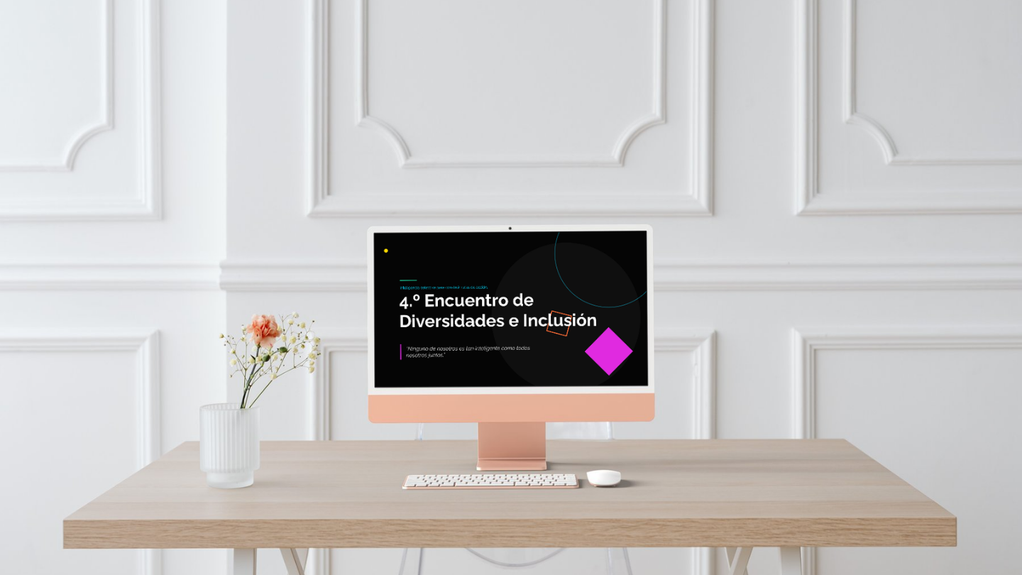 Computadora en un escritorio de madera con pantalla que muestra un cartel de evento titulado '4° Encuentro de Diversidades e Inclusión', junto a una planta con flores en un florero blanco.