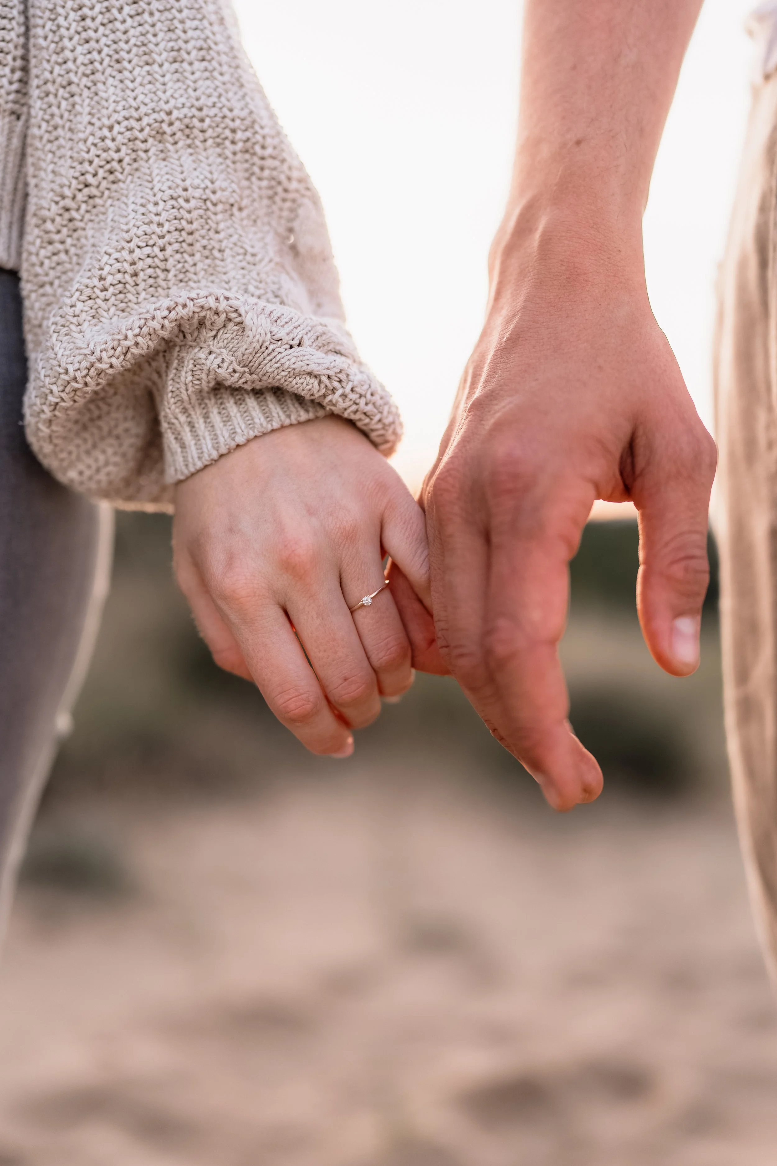 Paarshooting im Mainzer Sand – Detailaufnahme zweier Hände beim Händchenhalten, eingefangen im warmen Licht des Sonnenuntergangs.