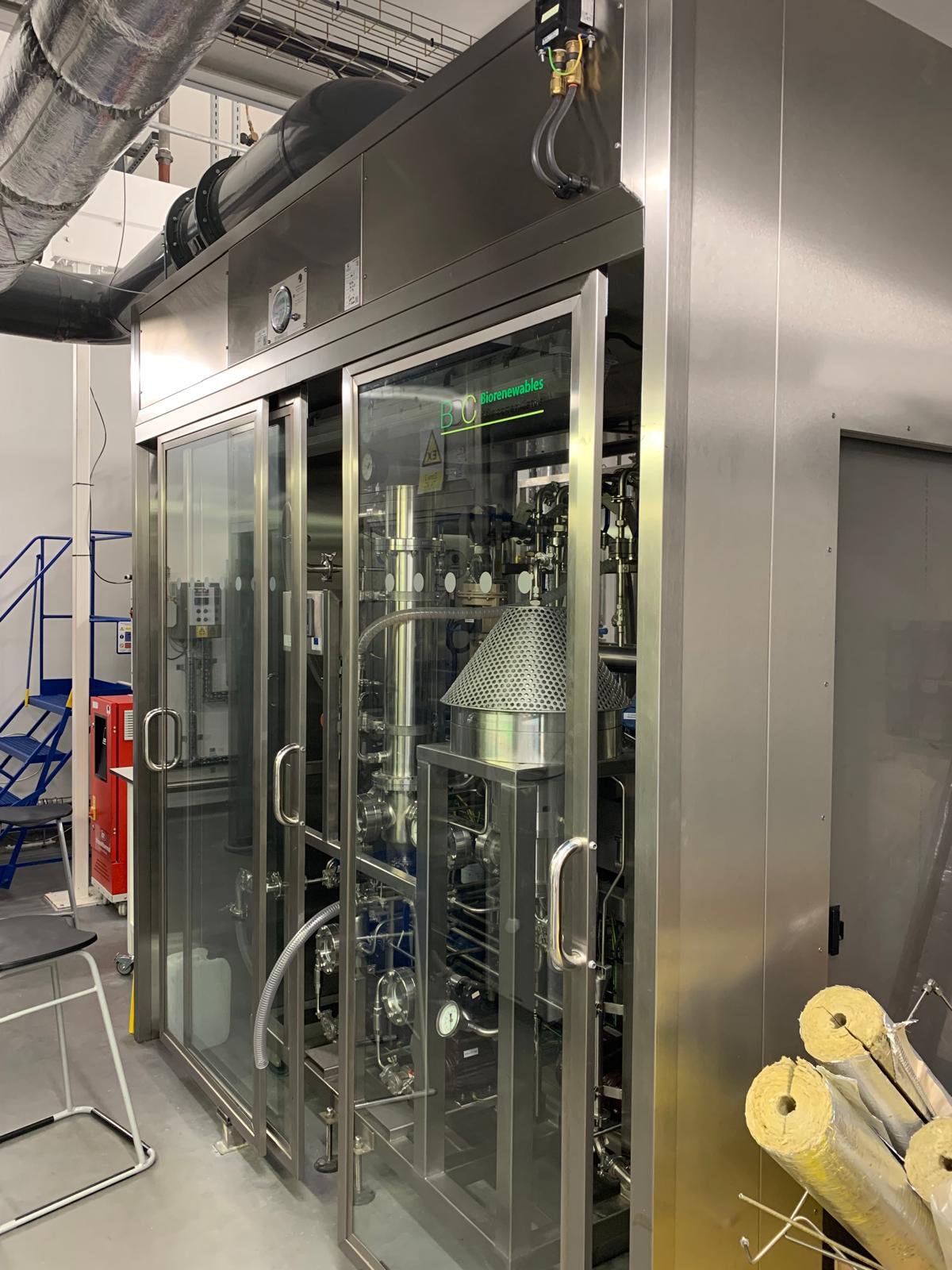 Industrial equipment in a laboratory or manufacturing facility with metal pipes and a glass enclosure
