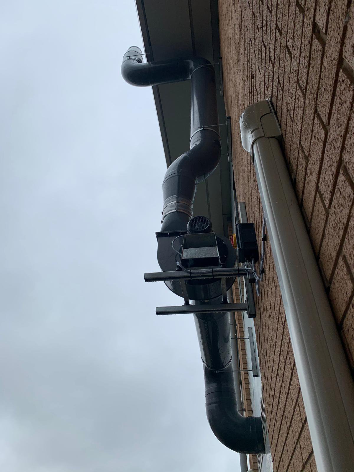 Exterior piping system attached to a brick wall, extending vertically and horizontally along the building.