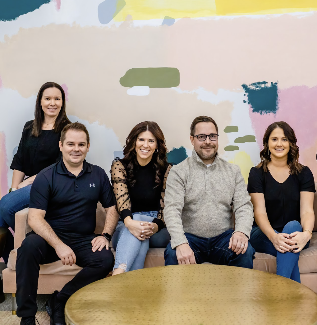 Group of five event professionals sitting and standing in a modern, colorful room with abstract wall art.