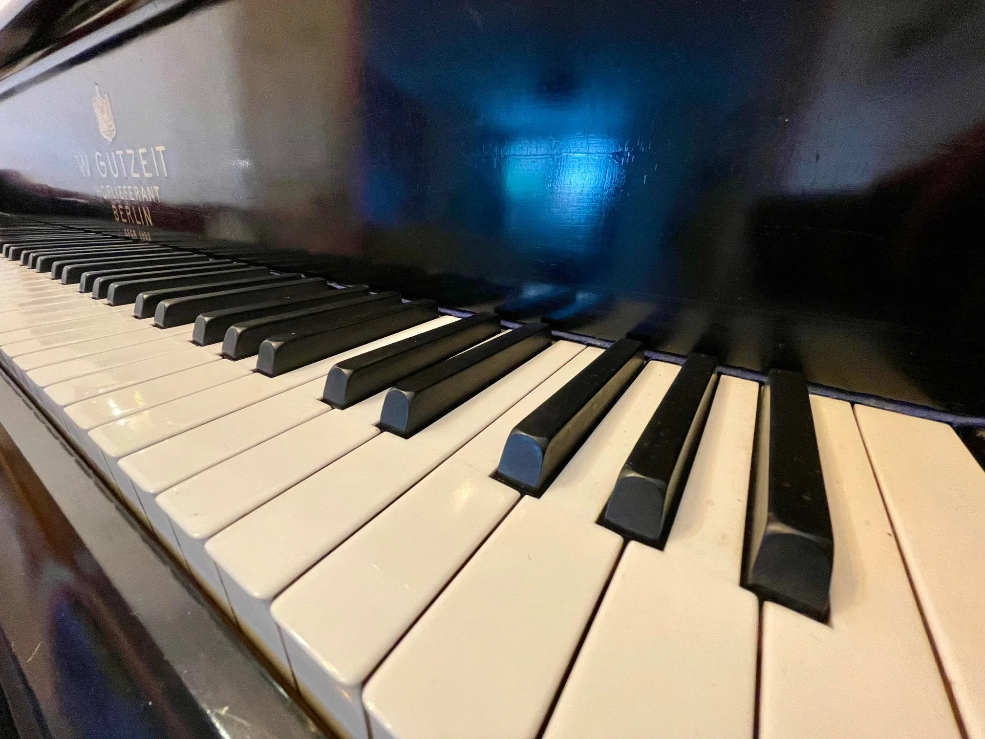 Close-up view of a piano keyboard with white and black keys, showing some signs of wear. The side of the piano has a label with the text 'W Gutzeit Hoboken Berlin'.