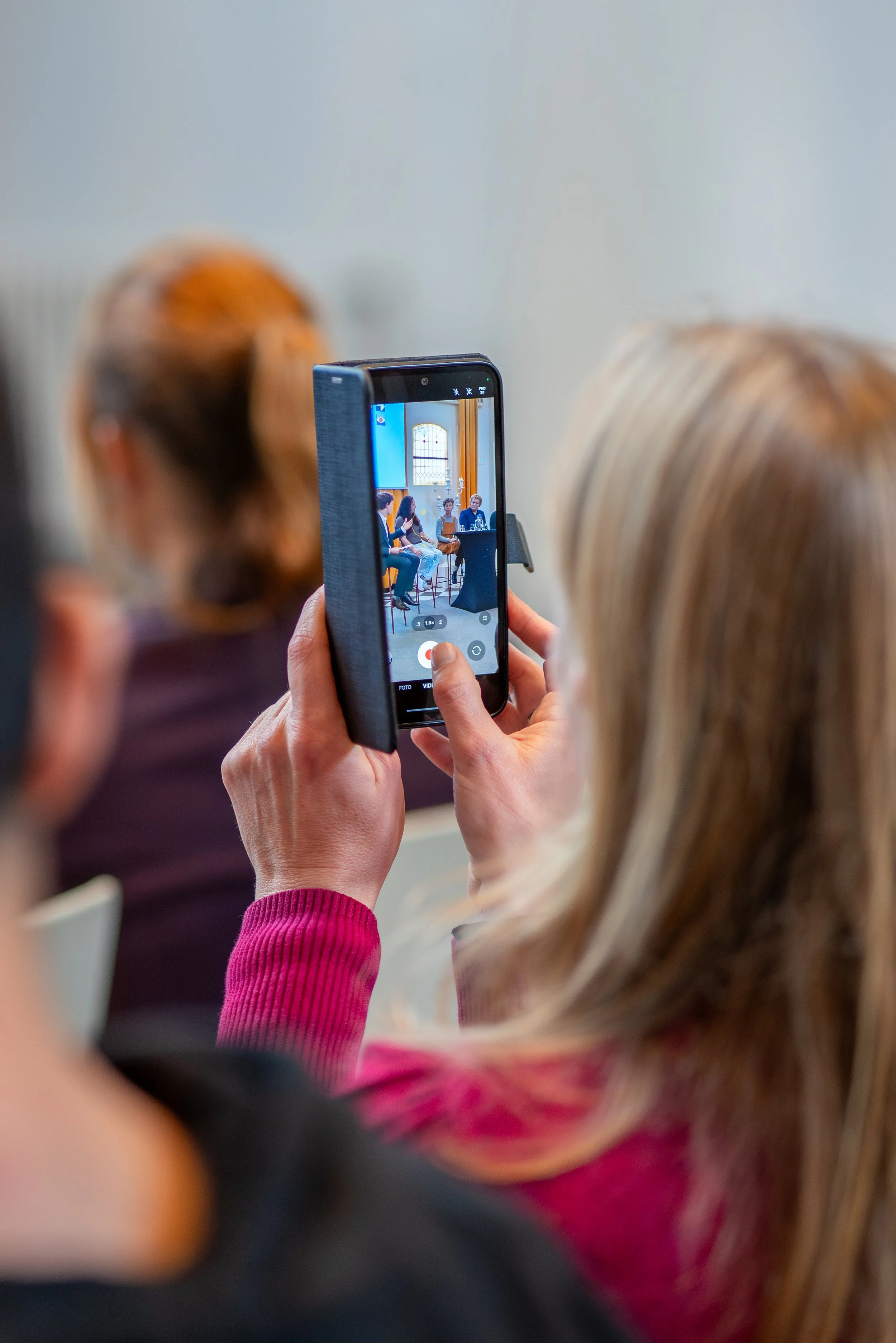 Person recording a panel discussion with their phone during an indoor event.