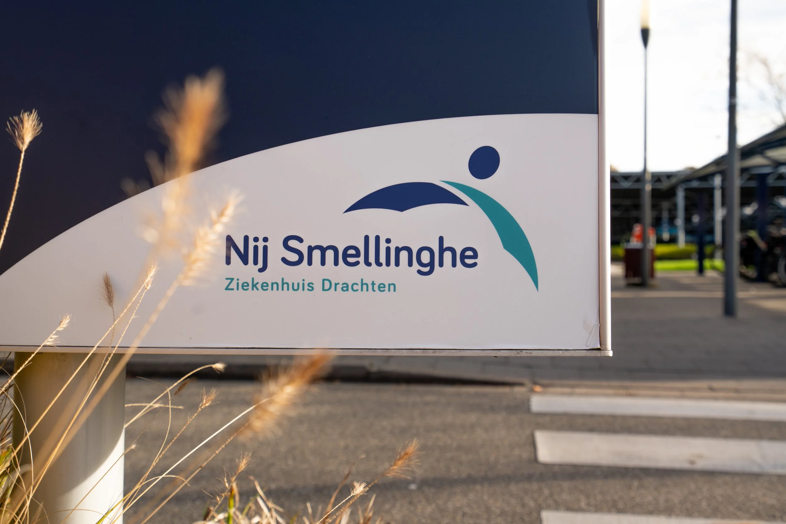 Hospital sign for Nij Smellinghe, Ziekenhuis Drachten, with a parking lot and cars in the background.