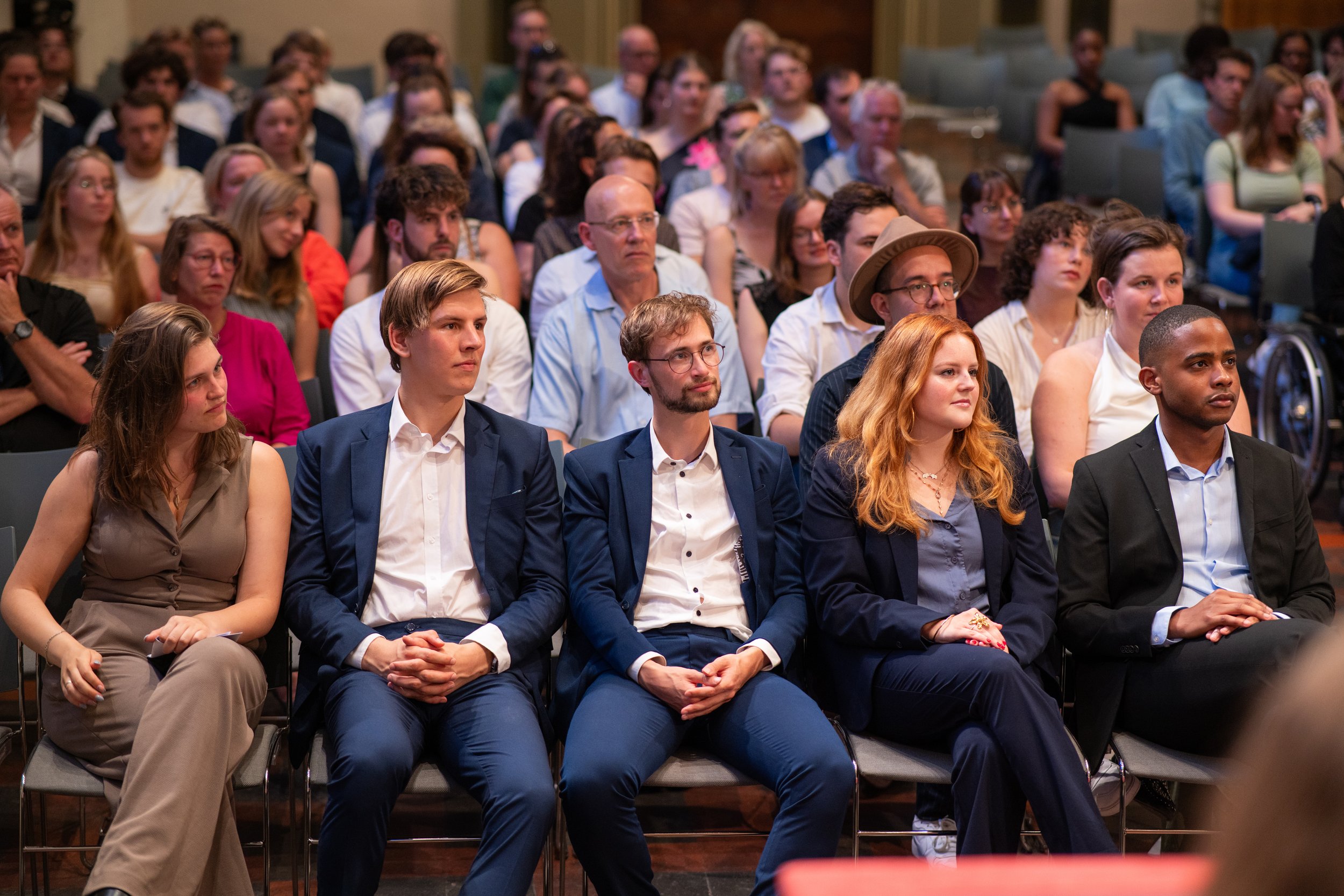 People attending a formal event or presentation, seated in rows, paying attention to the speaker or performance.