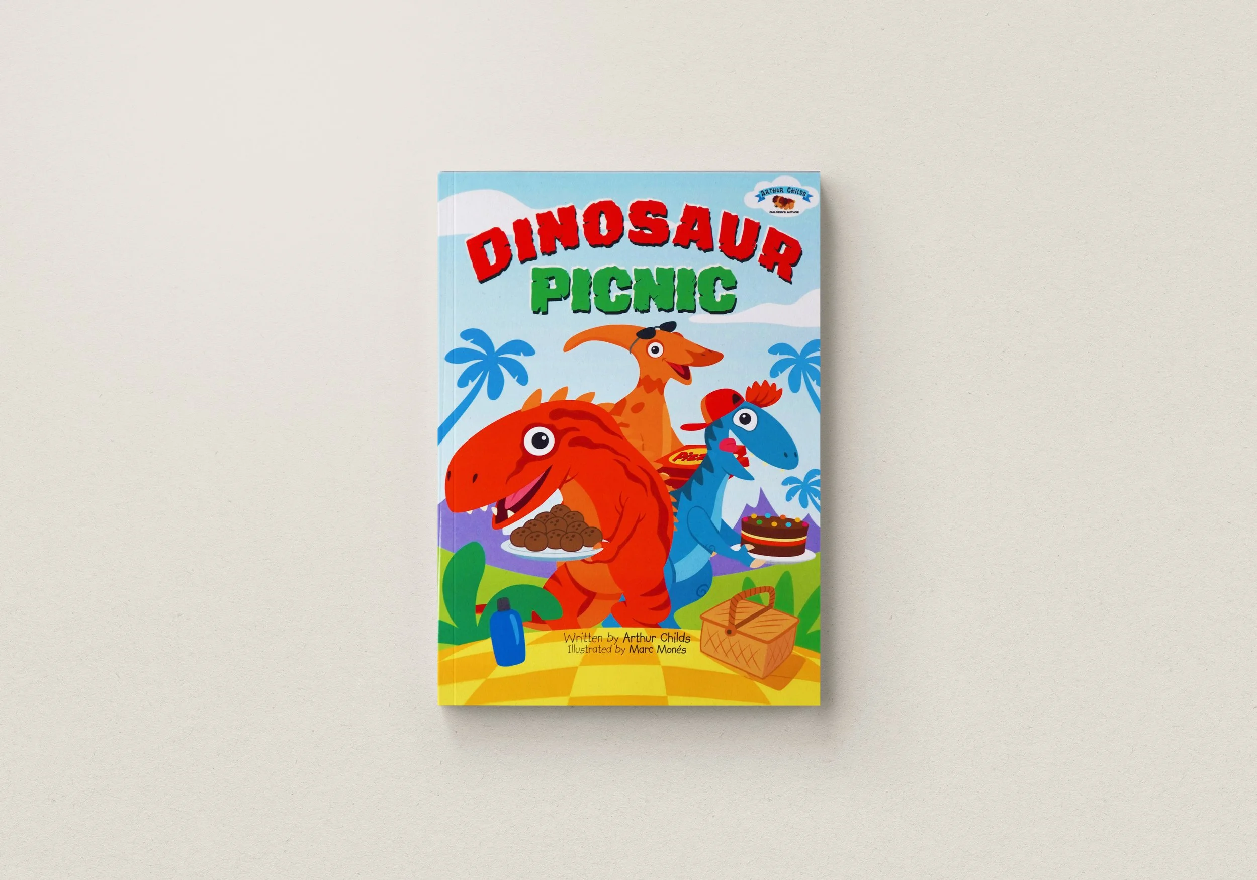 Cover of a children's book titled 'Dinosaur Picnic' featuring colorful cartoon dinosaurs holding picnic food, with palm trees and mountains in the background.