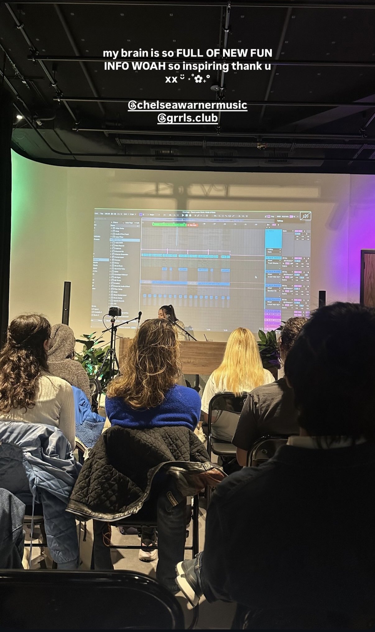Audience attending a music production workshop or class with a large screen displaying digital audio workstation software. A woman is seated at a piano in front of the screen. Overhead, white text indicates excitement and references Instagram tags.