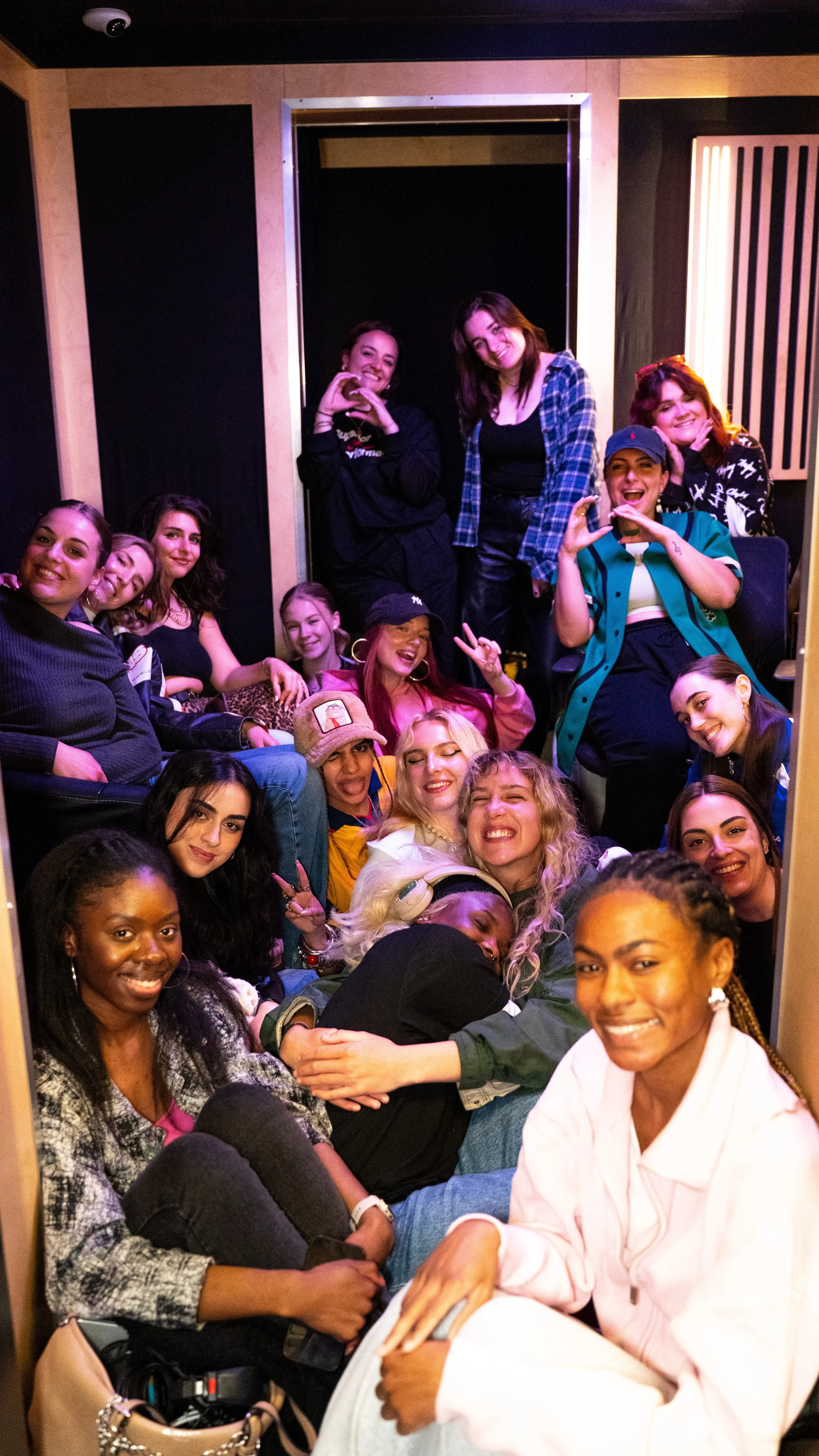 Group of women smiling and posing for group photo in a recording studio with black walls and acoustic panels.
