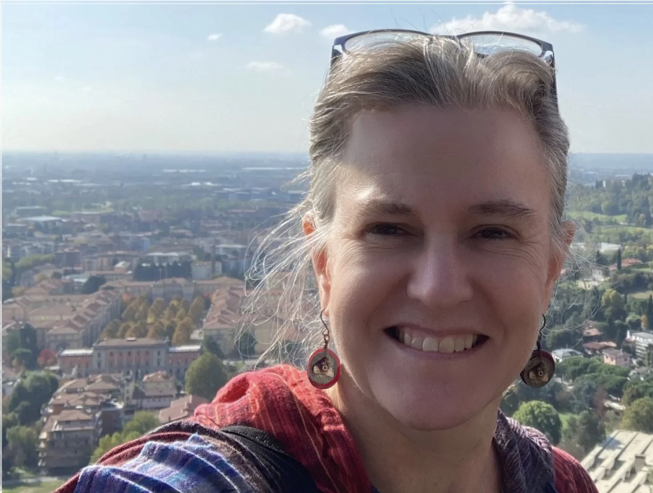 Headshot of Pastoria's Karen McCally, standing atop a high hill in Bergamo, Italy, with the town showing in the background.