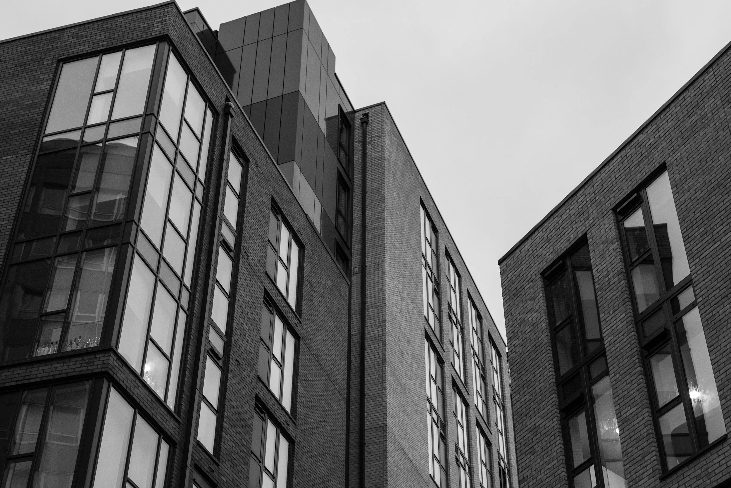 Black and white photo of modern multi-story urban buildings with brick and glass exteriors, viewed from below.