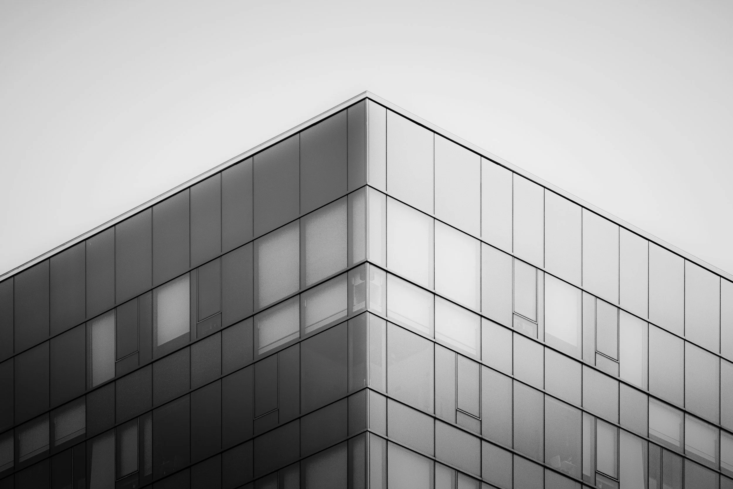 Black and white photo of the corner of a modern glass building with multiple windows.