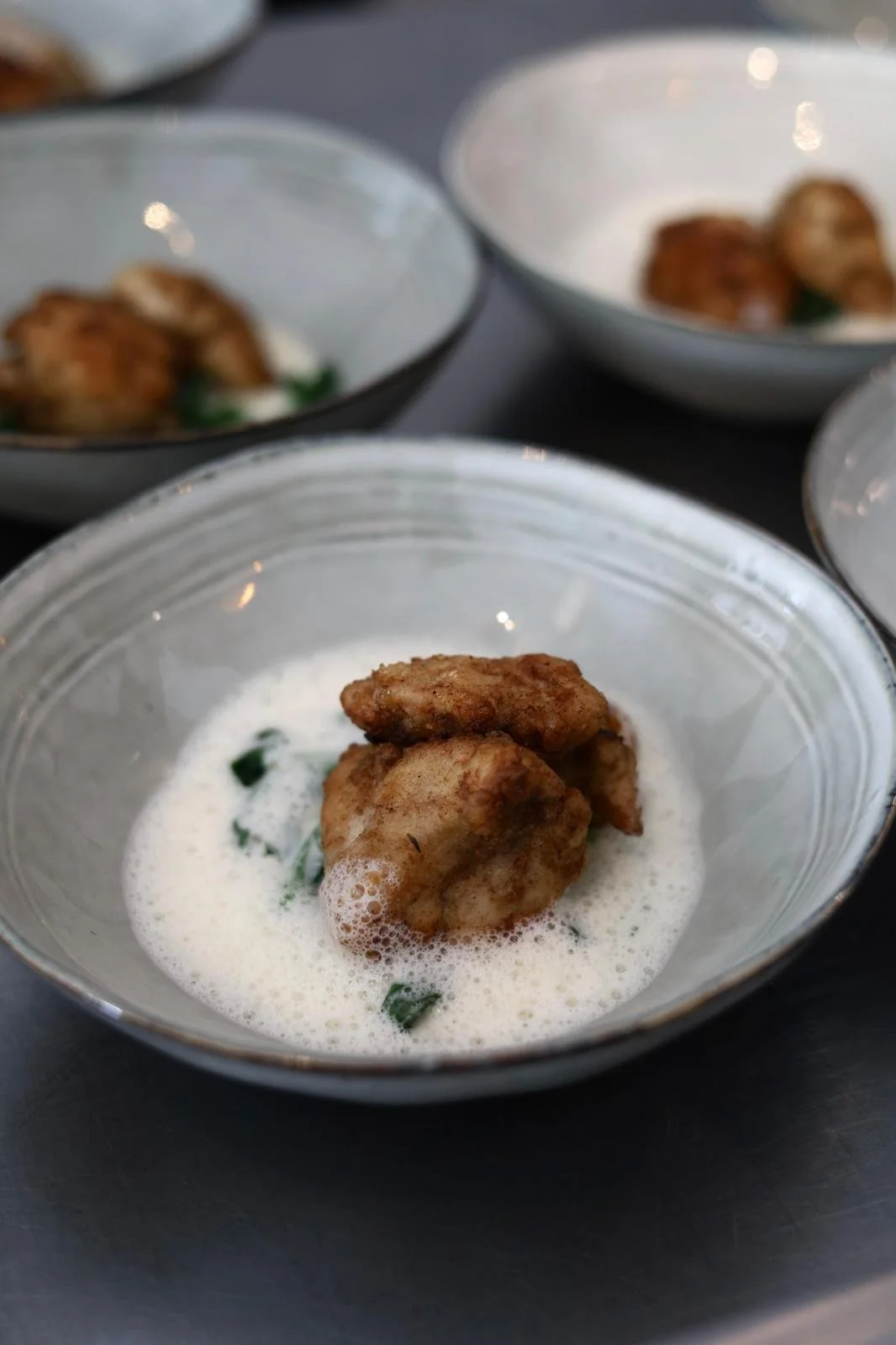 Fried chicken pieces served in a bowl with a creamy white sauce containing small herbs.