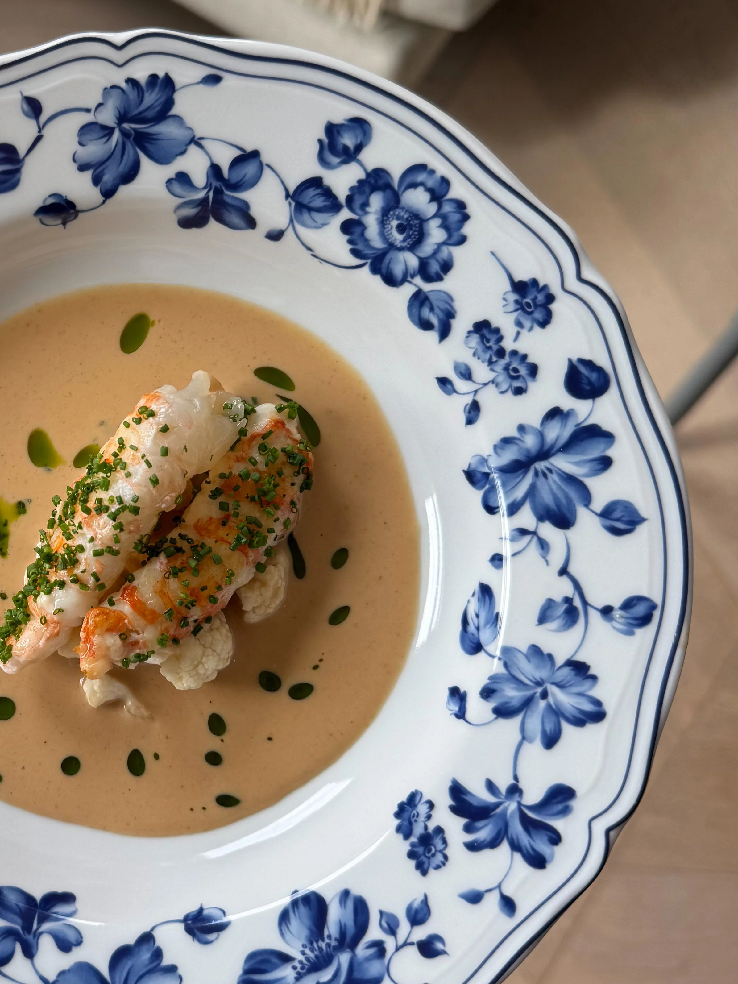A blue and white floral patterned bowl filled with creamy soup, garnished with chopped chives, a dollop of cream, and a small piece of seafood.