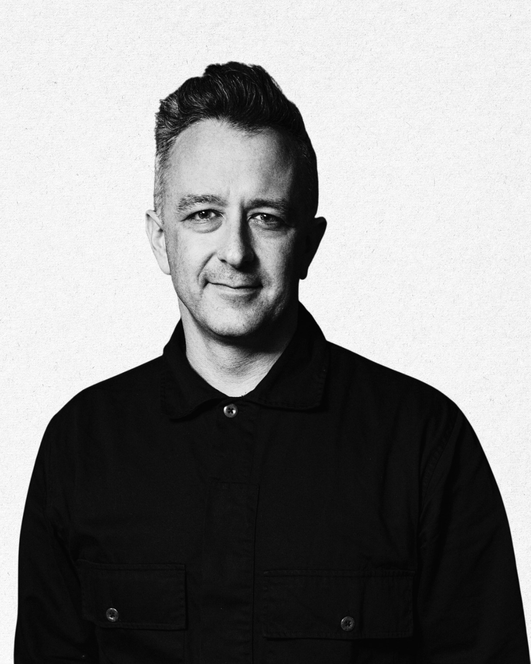 Black and white portrait of a man with short, styled hair, wearing a button-up shirt, smiling slightly, against a plain background.