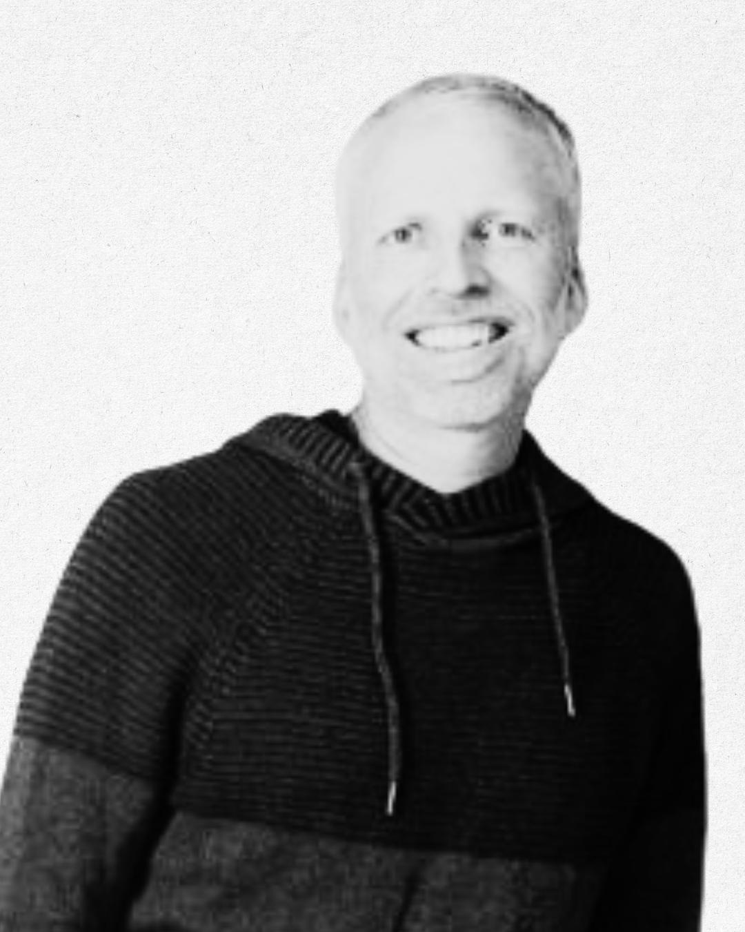 Black and white portrait of a smiling man wearing a striped hoodie with a plain background.