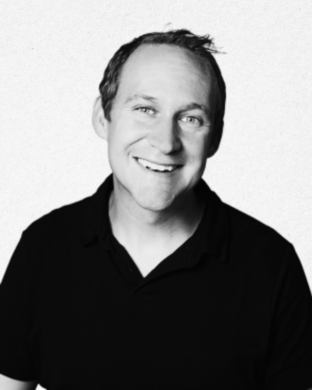 Black and white portrait of a smiling man with short dark hair, wearing a black shirt, against a plain background.