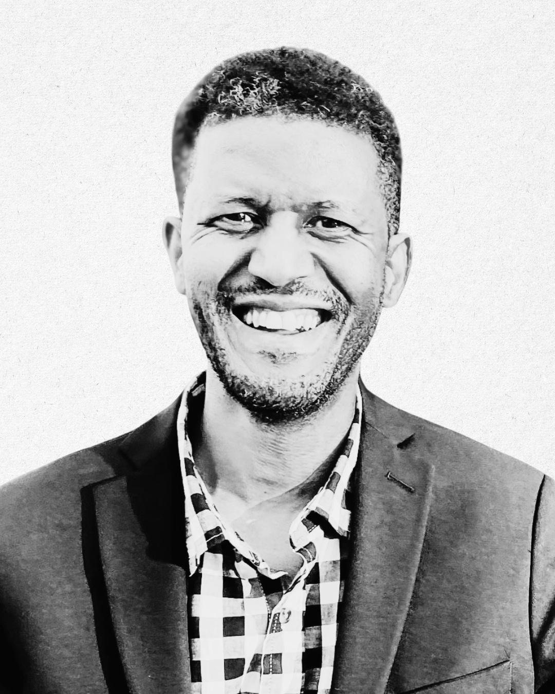 Black and white portrait of a smiling man wearing a checkered shirt and a blazer.