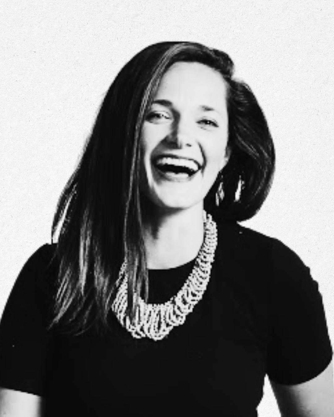 Black and white photo of a woman smiling, with long hair, wearing a black top and a chunky necklace.