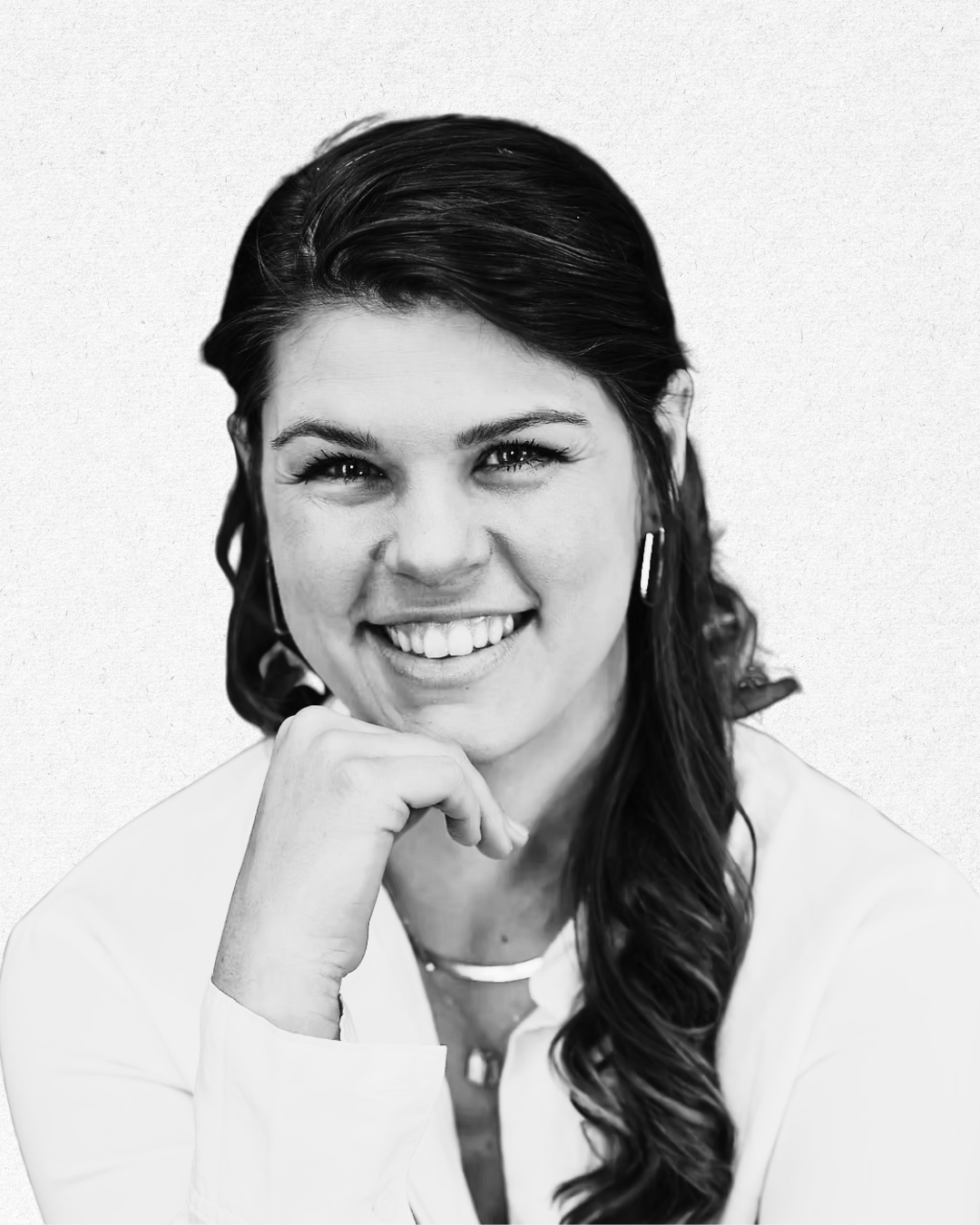 Black and white portrait of a smiling woman with dark hair, wearing earrings, a necklace, and a light-colored blouse, with her hand resting on her chin.