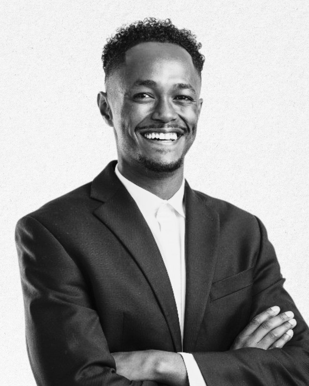 Black and white professional portrait of a smiling man in a suit with arms crossed.