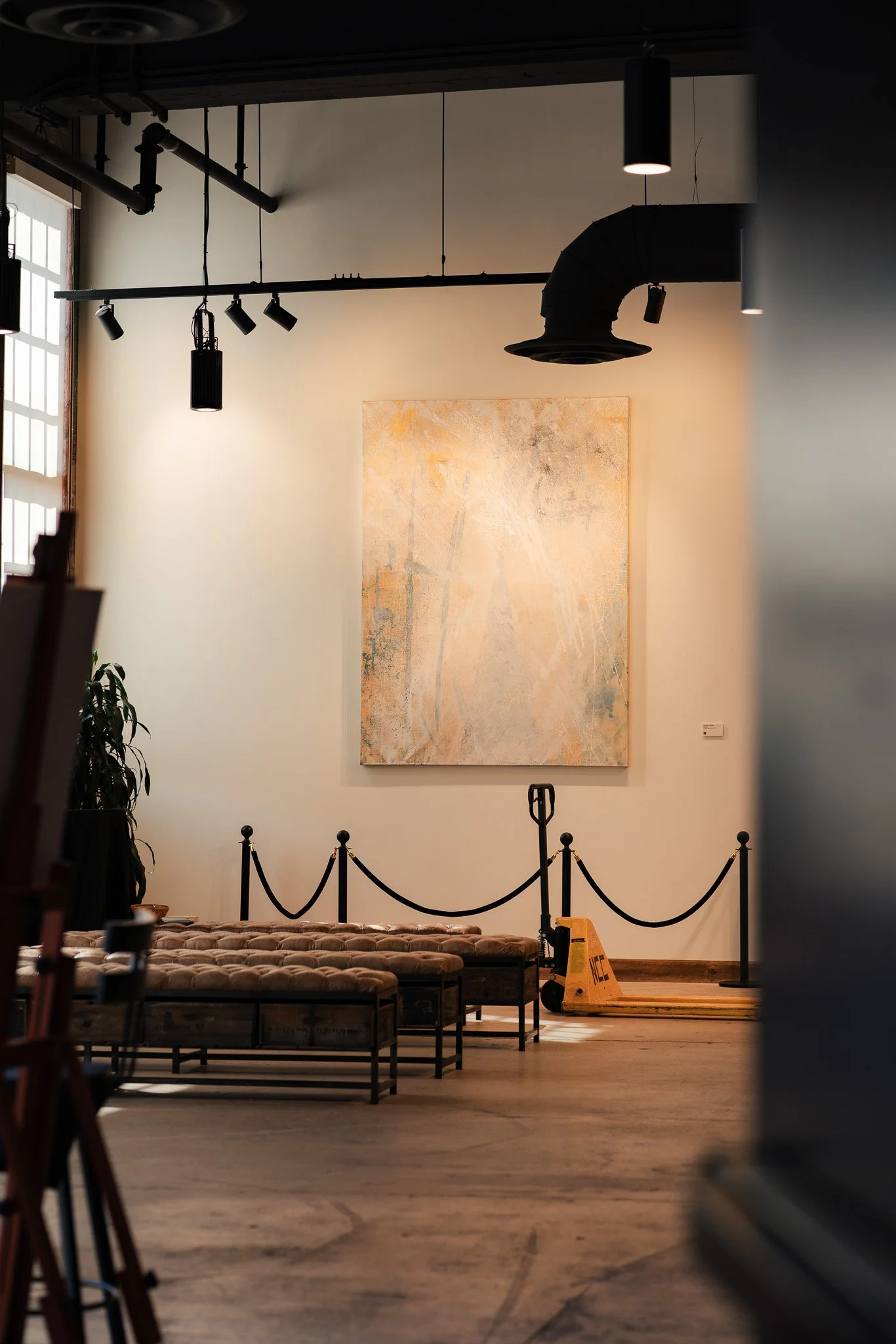 A bright, textured painting sits on a white wall in a gallery space with leather chairs
