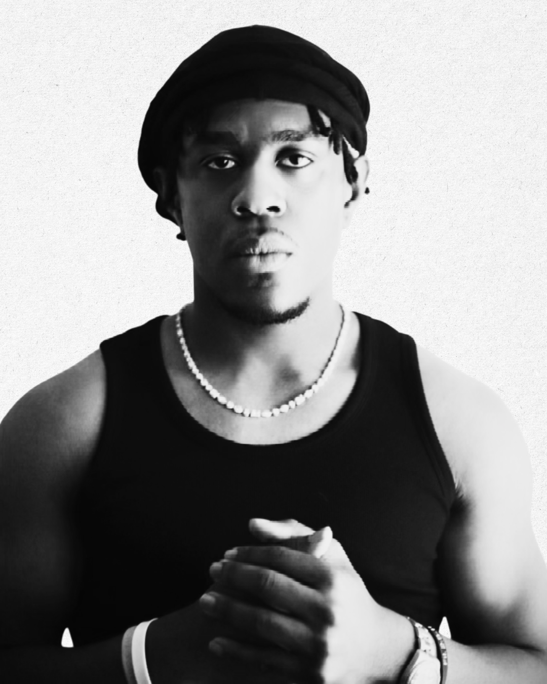 Black and white portrait of a young man with dreadlocks wearing a head wrap, necklace, and sleeveless shirt, standing against a plain background.
