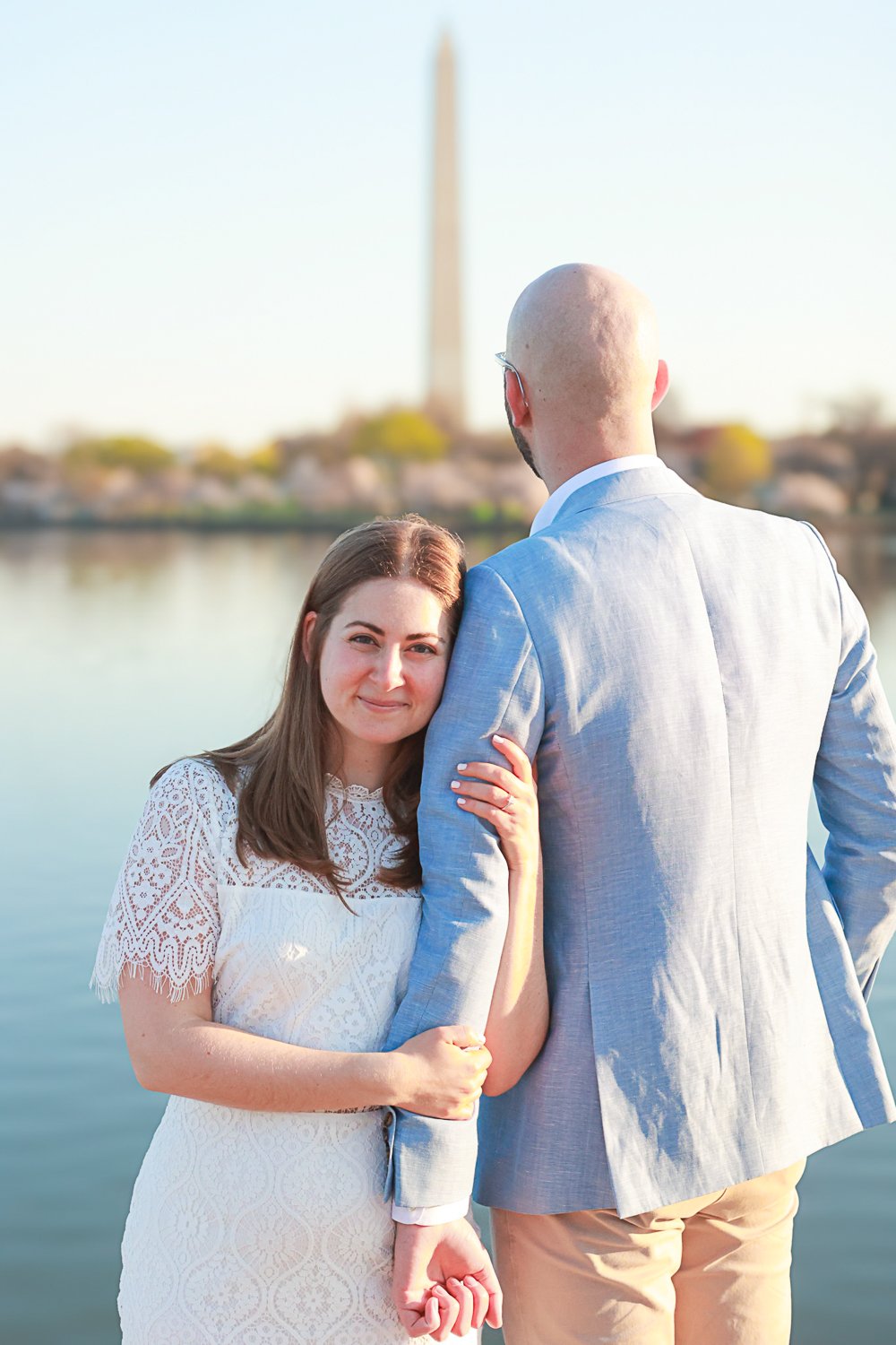 Couple posing near water with Washington Monument in background.