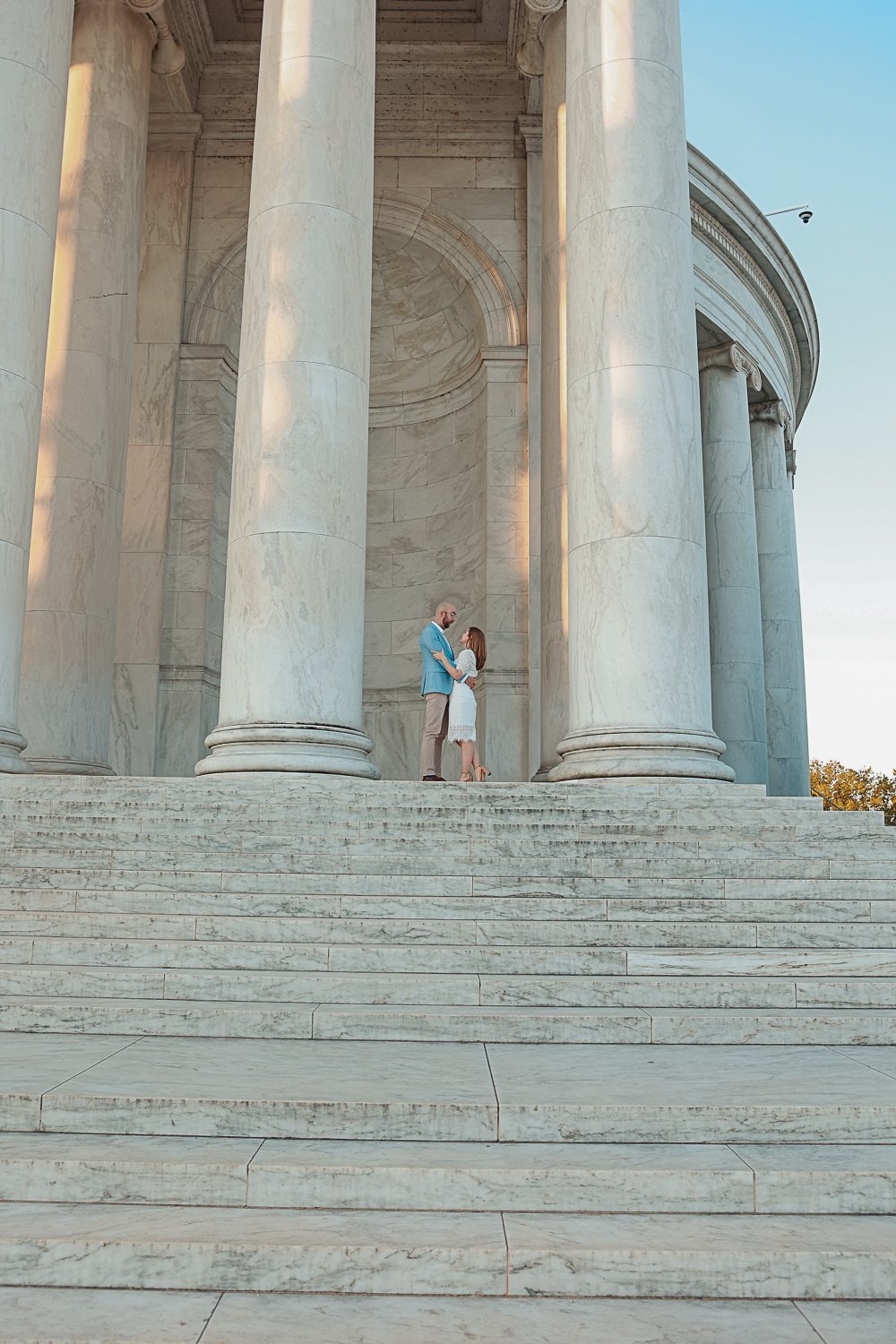 Couple embracing on marble steps of neoclassical building with large columns.