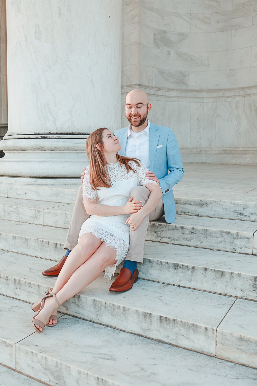 Couple sitting on marble steps, man in light blue suit, woman in white lace dress.