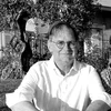 Black and white photo of a person in glasses standing outdoors with trees in the background.