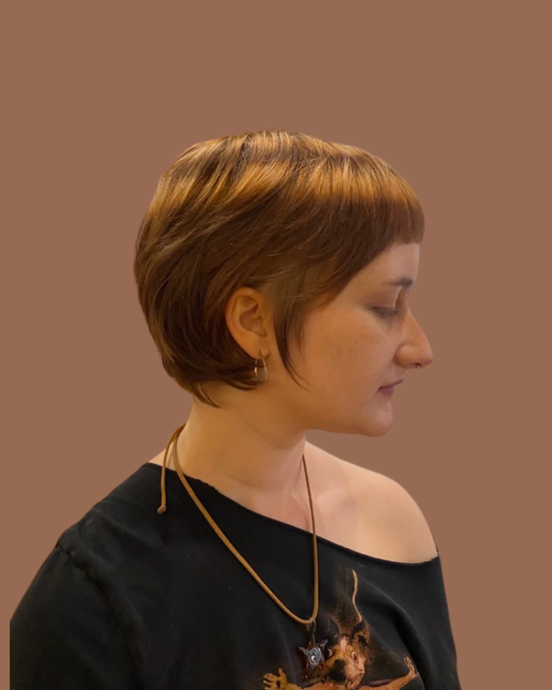 person with off shoulder black Tshirt faces sideways with short cropped red hair with blonde halo highlights on top of head