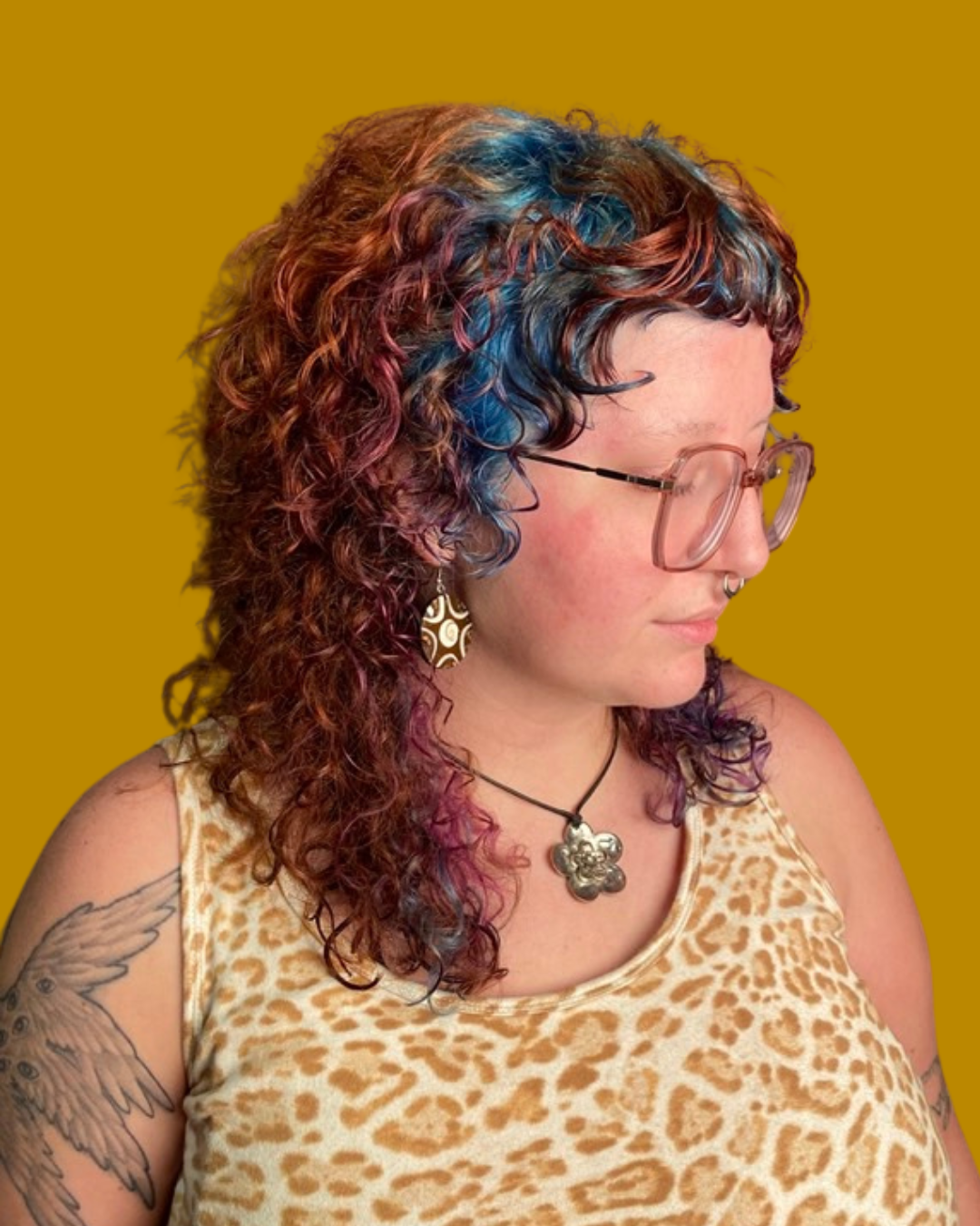 person with curly hair dyed copper blue and purple wearing glasses and leopard print shirt