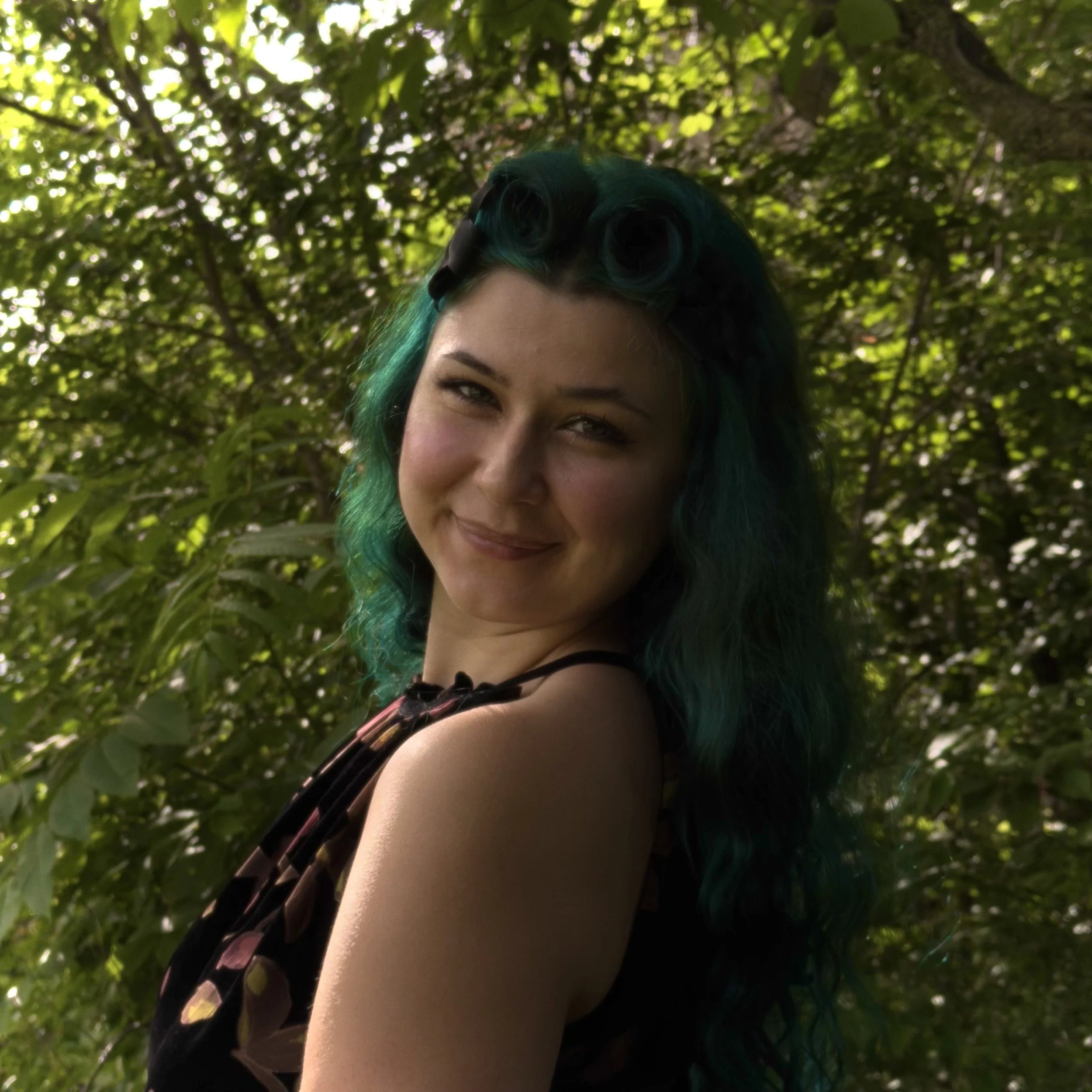 woman with green and brown hair standing in front of tree smiling at camera